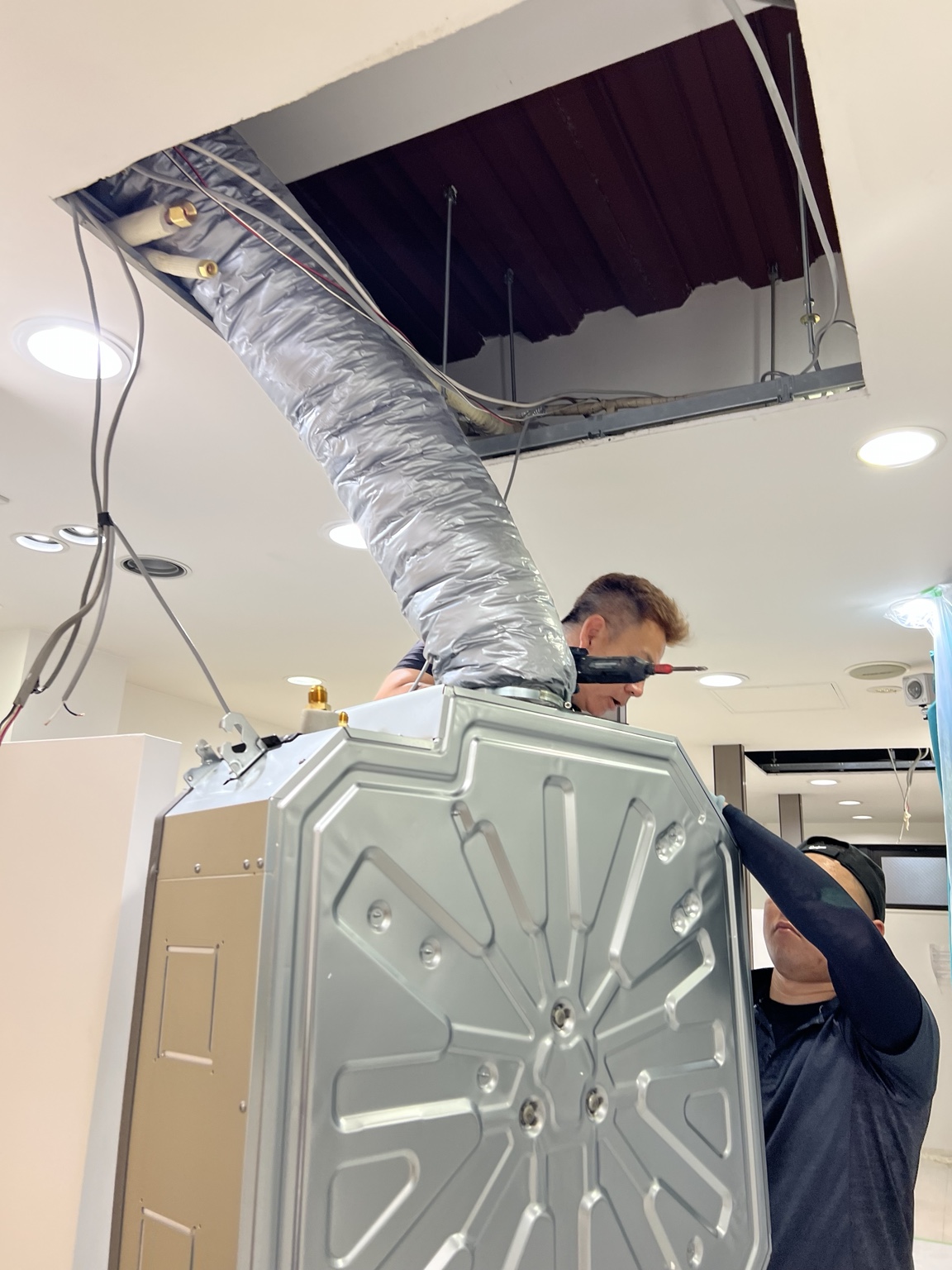 天井カセット形業務用エアコンの新しい室内機を吊り込む作業